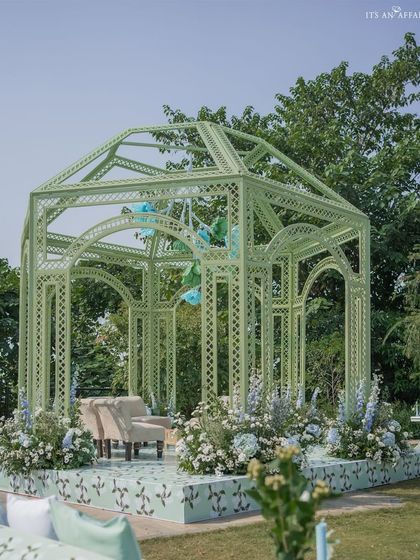 The mandap set on a stage with a custom-printed floral floor, surrounded by arrangements of delphiniums and hydrangeas.