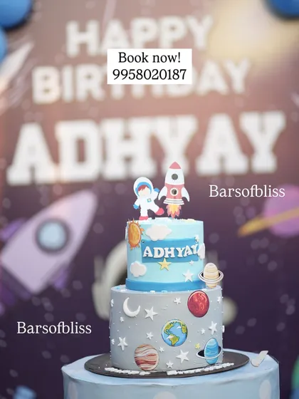 A custom two-tier cake for a space-themed birthday party. The cake is decorated with planets, stars, a rocket, and an astronaut, perfectly matching the party's decor.