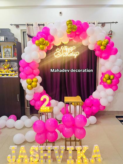 A vibrant pink and white circular balloon arch for a second birthday. This home setup includes a 'Happy Birthday' neon sign and the child's name in large light-up letters, creating a bright and cheerful photo spot.