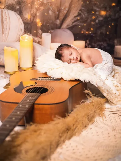 Another angle of the musician-themed newborn shoot, with the baby sleeping on a fluffy rug atop a guitar.