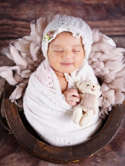 A sleeping newborn in a rustic bowl, holding a tiny teddy bear. This classic newborn pose is always a favorite for parents.