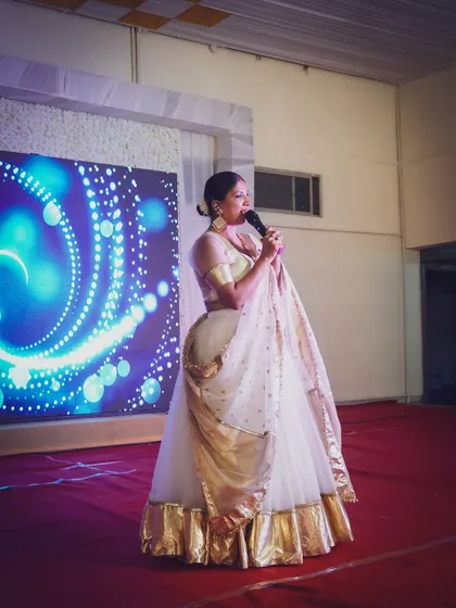 Here I am on stage in a classic white and gold lehenga, engaging the audience during a Sangeet. The LED screen behind me adds a dynamic visual element.