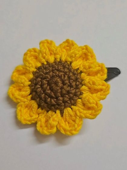 Another angle of the sunflower hair clip, showing its bright yellow petals and rich brown center. It's attached to a simple snap clip, making it easy to wear.