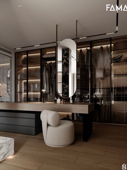 This design integrates a floating vanity directly into the walk-in closet system. The hanging oval mirror and modern stool create a chic spot for getting ready, surrounded by smoked glass wardrobes that showcase the clothing within.