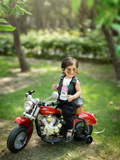 A cool biker girl with attitude. The combination of a leather vest, sunglasses, and a toy motorcycle makes for an unforgettable outdoor photoshoot.