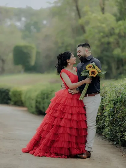 A beautiful pose during a pre-wedding session in a Pune garden. The woman's vibrant red dress stands out against the green foliage, creating a visually stunning and romantic photograph.