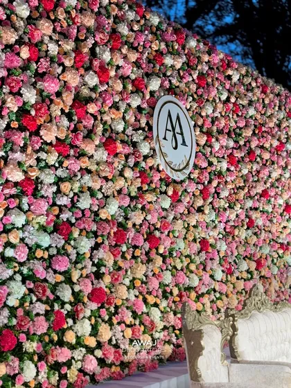 A close-up of the immense flower wall, showcasing thousands of fresh roses in shades of pink, red, and cream, with the couple's monogram at its center.