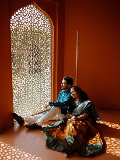 The couple sits by an ornate window, the sunlight casting beautiful geometric patterns on the floor. This quiet, contemplative moment is full of warmth and artistic beauty, perfect for a heritage-themed shoot.