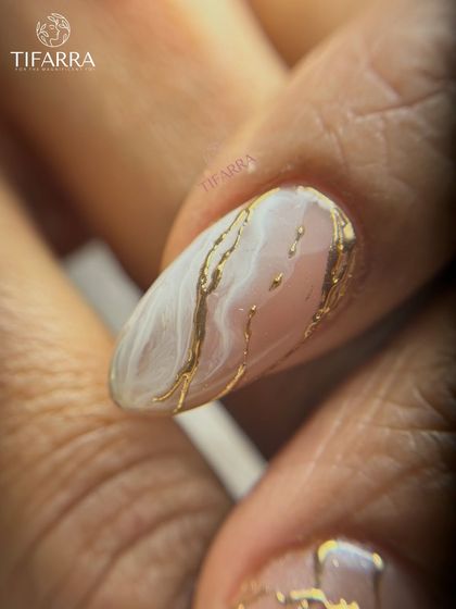 A detailed view of a white marble nail with delicate veins of molten gold running through it, creating a luxurious stone effect.