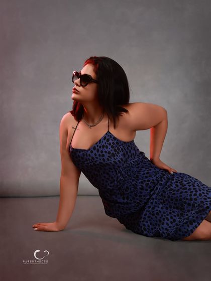 A dynamic pose on the studio floor, creating a sense of movement and editorial flair. The lighting highlights the texture of the dress and the subject's confident posture.