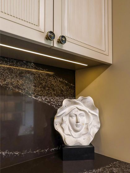 Art and function coexist beautifully in our designs. This detail shot shows a unique sculptural piece against the dark marble backsplash, illuminated by a warm under-cabinet LED strip, proving that even practical spaces can be personalized with artistic touches.