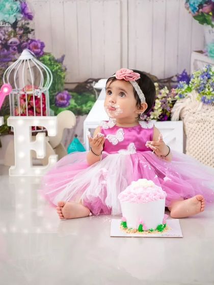A full view of the pink and purple floral cake smash setup. The light-up 'ONE' and '1' props clearly mark this important milestone.