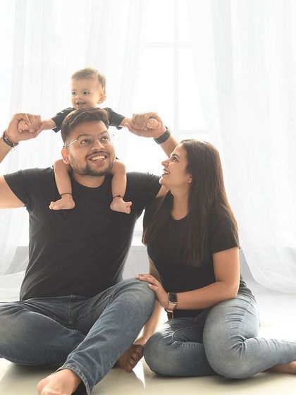 A fun family portrait with a toddler perched on dad's shoulders. The coordinated black shirts and jeans give this studio photo a casual and contemporary feel.