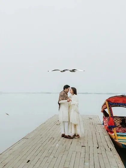 An intimate moment on a quiet dock in Kashmir, with birds flying overhead against a misty, minimalist landscape. This image captures the serene, fairytale-like atmosphere of our destination pre-wedding shoots.