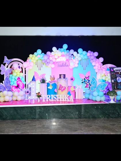 A full stage setup for a rainbow butterfly theme. The backdrop features pastel-colored panels and butterfly accents, all tied together with a multi-colored balloon garland.