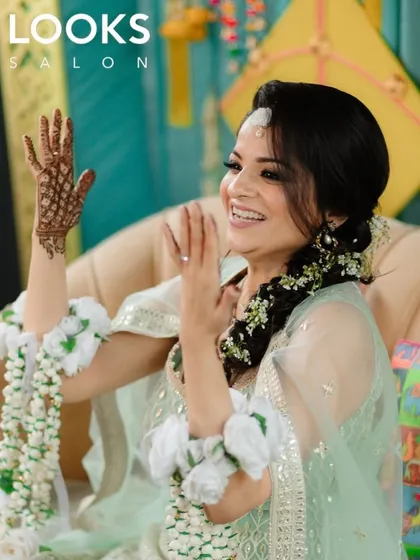 A bride-to-be glowing for her Haldi or Mehendi ceremony. Her makeup is fresh and radiant, paired with a beautiful floral hairstyle that is perfect for daytime wedding events.