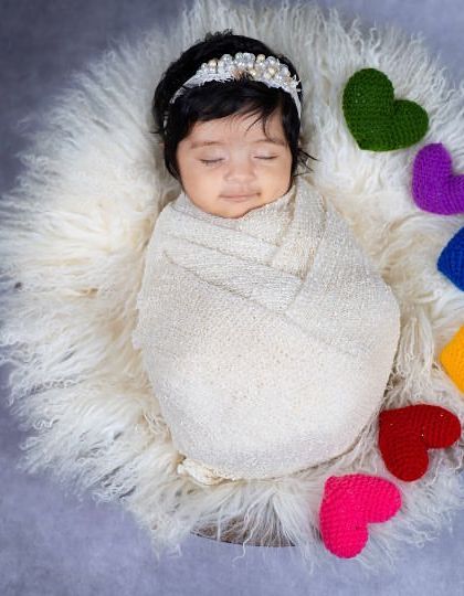 A beautiful overhead shot of a swaddled newborn surrounded by a rainbow of felted hearts. This composition is simple, colorful, and full of love, creating a perfect birth announcement photo.