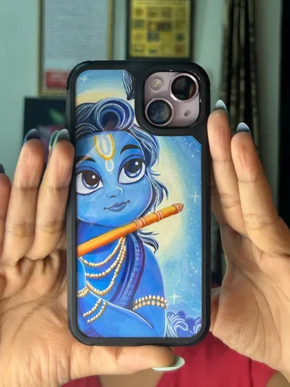 Holding up a finished Krishna phone cover to show how it looks in hand. The artwork is vibrant and fits snugly within the protective case, making it a durable and beautiful piece of everyday art.
