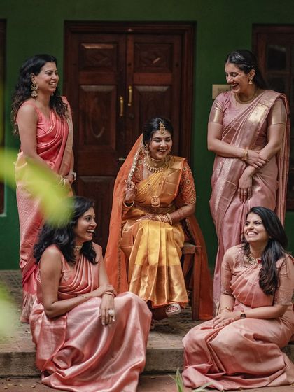 A bride and her bridesmaids share a laugh, all dressed in coordinated pastel sarees.