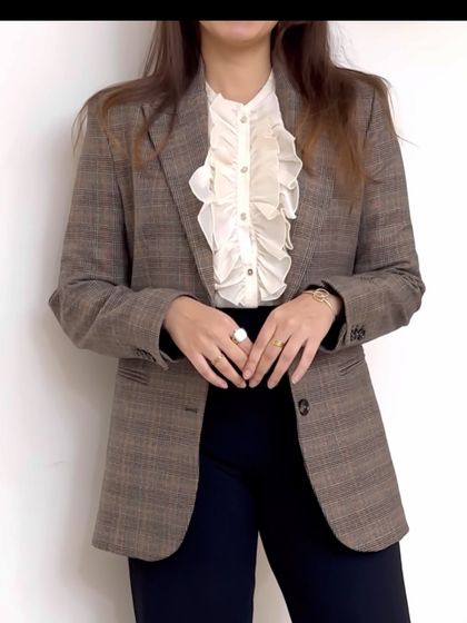 A classic workwear combination. This checked brown blazer paired with a ruffled white shirt and dark trousers is a perfect example of a polished, professional look with a touch of texture and personality.