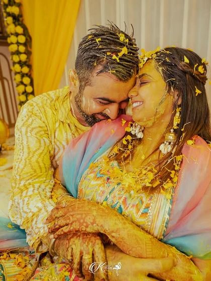 A candid, joyful moment of a couple embracing during their haldi ceremony, both covered in paste and petals.
