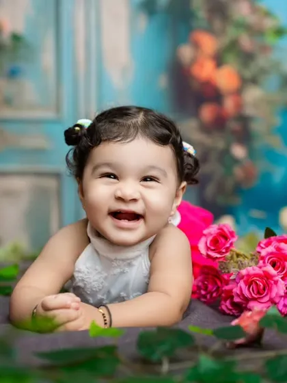 A happy baby girl with the cutest pigtails, lying in a field of flowers. Her joyful expression is the focus of this colorful portrait.