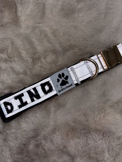 A flat-lay of the custom 'Dino' collar on a soft, furry background. This view highlights the quality of the embroidery and the sturdy collar hardware.