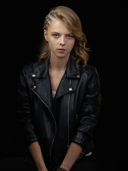 A powerful portrait of a model in a black leather jacket against a solid black background, creating a moody and intense atmosphere.