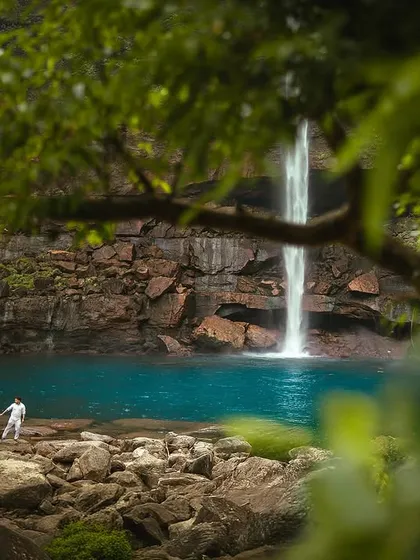 A wide, scenic view of the couple standing by the waterfall, emphasizing the grand scale of the landscape. This kind of shot establishes the epic, destination feel of your pre-wedding story.