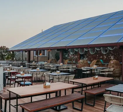 An expansive view of the rooftop terrace, showing the variety of seating arrangements, from picnic-style benches to smaller tables. This flexibility allows the space to accommodate both large groups and intimate gatherings.
