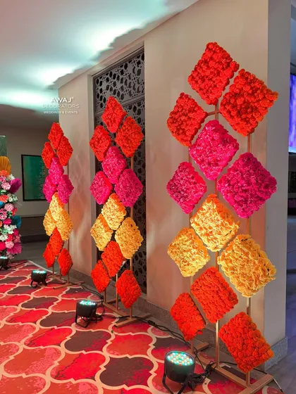 Geometric floral stands made of marigolds in shades of orange, yellow, and pink, creating a modern yet traditional entrance.