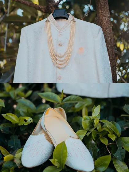 A detail shot of the groom's wedding attire, showcasing his elegant sherwani, pearl necklace, and traditional shoes (juttis).