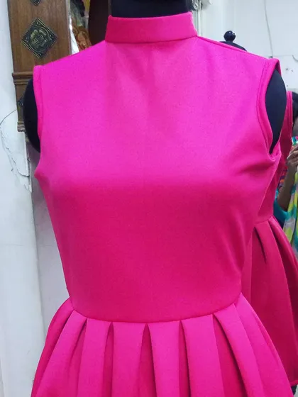 A chic and modern party dress in a stunning fuchsia pink. The high neck and pleated peplum skirt create a sharp, stylish silhouette for any celebration.
