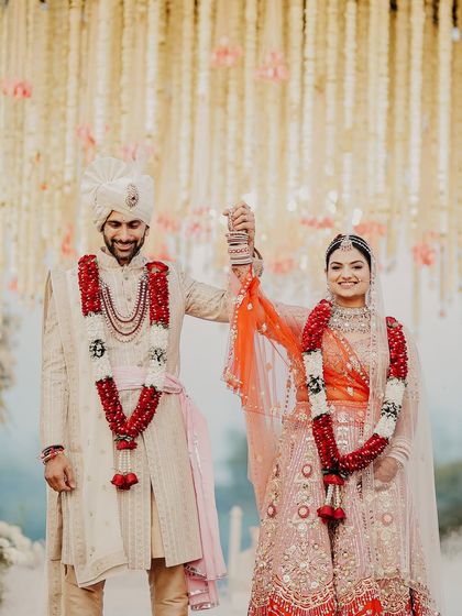 A moment of triumph and togetherness after the Varmala. The couple holds hands, celebrating their union under a breathtaking canopy of flowers.