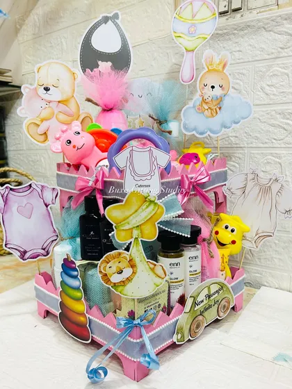 A heart-shaped tiered hamper overflowing with essentials for the baby and treats for the parents-to-be, decorated with cute, playful cutouts.