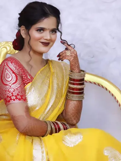 A North Indian bride in a vibrant yellow saree, her look completed with a bold lip and traditional red and white bangles.