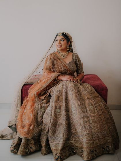 A regal portrait of the bride seated, her heavily embroidered lehenga spread out beautifully. She looks away with a graceful and poised expression.