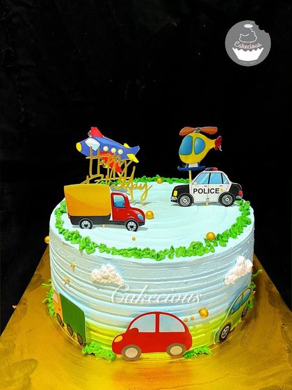 A cake for a little one who loves all things that go. This transportation-themed cake is decorated with a car, truck, airplane, and helicopter, ready to drive into a happy celebration.