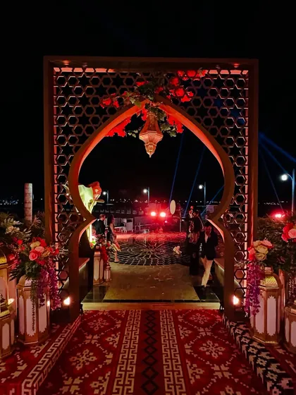 An opulent entrance for a celebration in Doha, glowing under the night sky. The design features intricate latticework, golden lanterns, and a traditional patterned rug. ⭐️