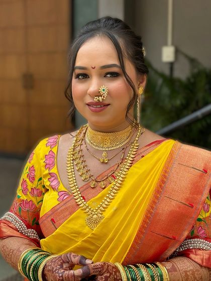 A classic Maharashtrian bridal portrait. The makeup is perfectly balanced with the heavy gold jewelry and the vibrant yellow saree, featuring a clean base and defined eyes.