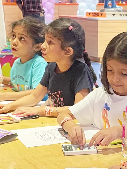 Young girls focus on their coloring sheets during the Janmashtami craft session.