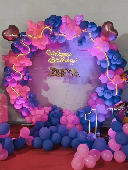A Barbie-themed first birthday with a pink and purple balloon ring and a "Happy Birthday" neon sign.