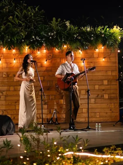 A simple wooden stage backdrop with string lights, perfect for live music performances at an outdoor reception.