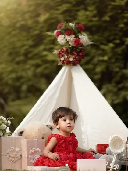 A thoughtful moment in a whimsical garden setting. This little girl looks so sweet and serene in her red dress, surrounded by flowers and teddy bears.