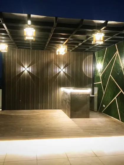 The same pergola at night. The space comes alive with hanging lanterns, wall sconces, and strip lighting under the deck and bar counter.