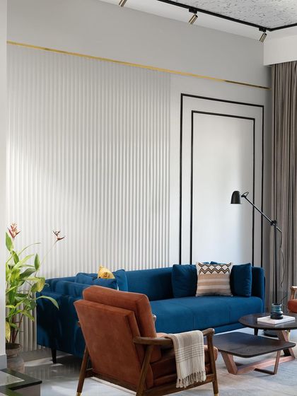 A wider view of the living room with the blue sofa, showing the full effect of the textured wall panels and contemporary track lighting.