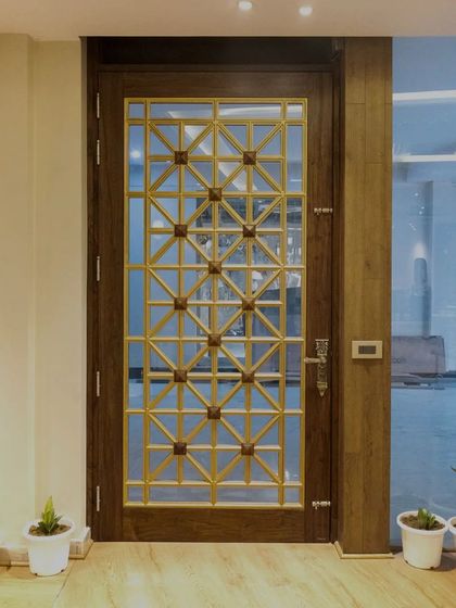 A beautiful example of a solid wood door combined with a detailed MDF 'jali' and glass. The golden finish on the 'jali' contrasts beautifully with the dark wood, creating a secure yet decorative main door.