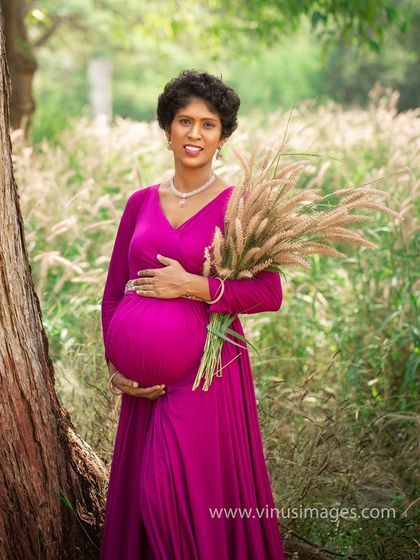 A solo portrait of the mother-to-be in a vibrant magenta gown, standing in a field of tall grass. The natural setting and her confident pose create a powerful and beautiful image.