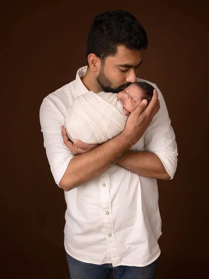 A father's tender kiss for his newborn. This classic studio portrait, with its simple background, focuses entirely on the emotional bond between father and child.