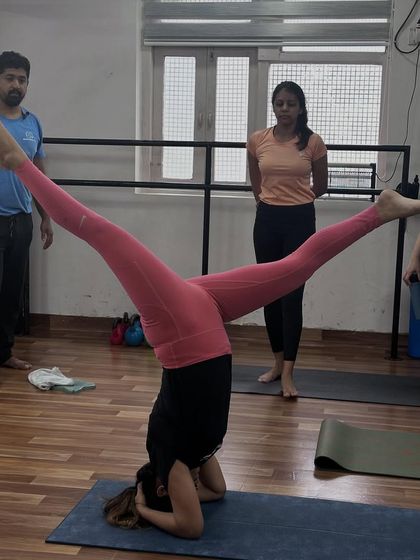 A student performs Upavistha Konasana (Wide-Angled Seated Forward Bend) in a headstand, a challenging variation requiring core strength and balance.